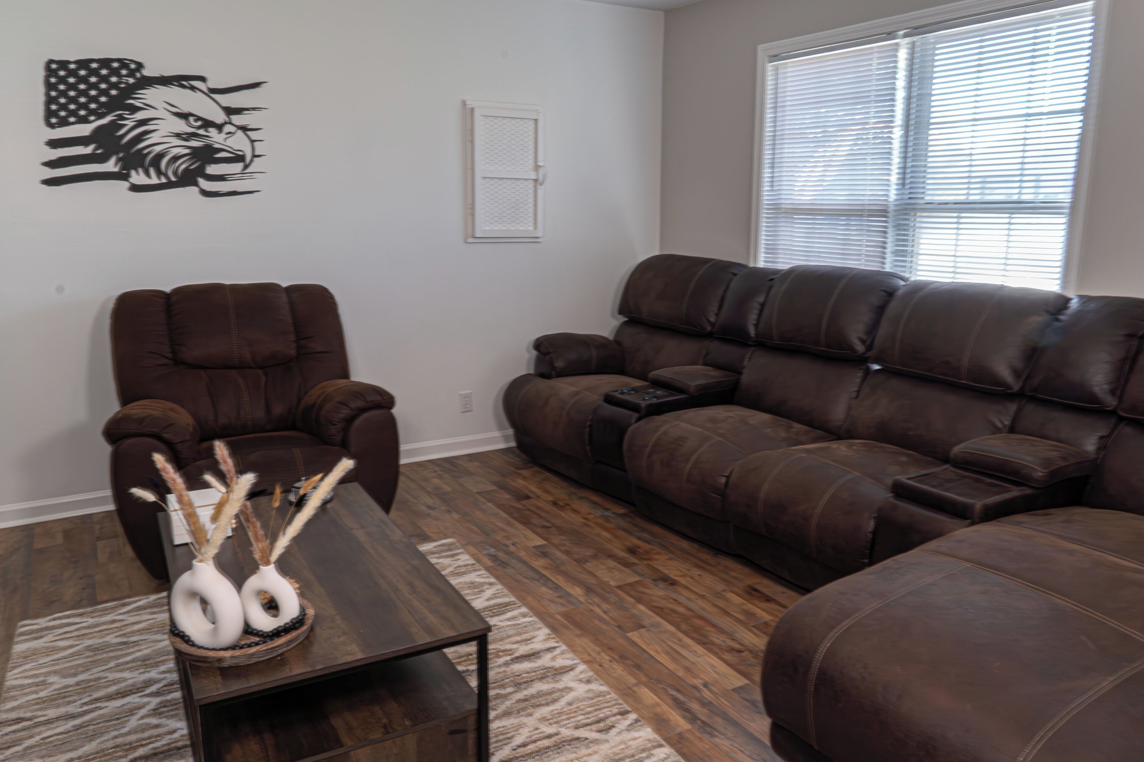 A living room with a brown leather sofa, a brown leather chair, and a wooden coffee table with decorative vases.