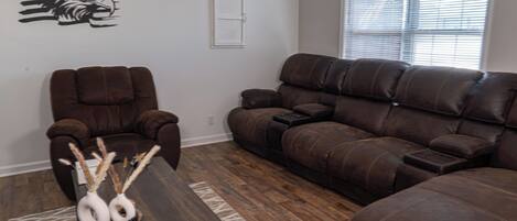 A living room with a brown leather sofa, a brown leather chair, and a wooden coffee table with decorative vases.