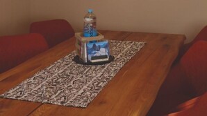 A dining area with a wooden table, red cushioned chairs, a patterned rug, a water bottle, and a painting of a cow. - Cosy apartment for 4 people with WIFI, TV and balcony (Fuhre)