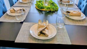 Une table à manger dressée pour quatre personnes, avec vue sur un paysage verdoyant grâce à de grandes fenêtres.