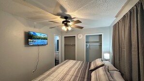 A bedroom with a bed, a ceiling fan, a TV, a clock, and a closet.