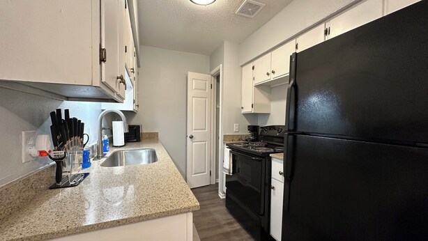 A kitchen with white cabinets, a black refrigerator, a stainless steel sink, and a stove.