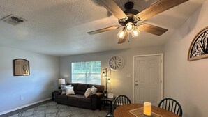 A dining area with a wooden table, chairs, a candle, a clock, and a ceiling fan.