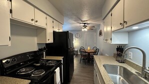 A kitchen with white cabinets, a black stove, a refrigerator, a dining table with chairs, and a sink.