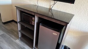 A compact living space with a flat-screen TV mounted on a wall, a small refrigerator, and a trash bin. - CourtesyStay (Mansfield)