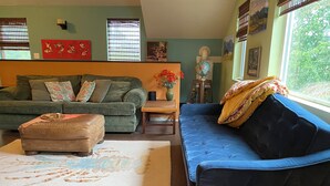 A living room with a green sofa, a blue sofa, a brown ottoman, and a small table with a vase of flowers. - Cozy 1-bedroom stand alone apartment in fantastic Missoula, MT.!!! (Missoula)
