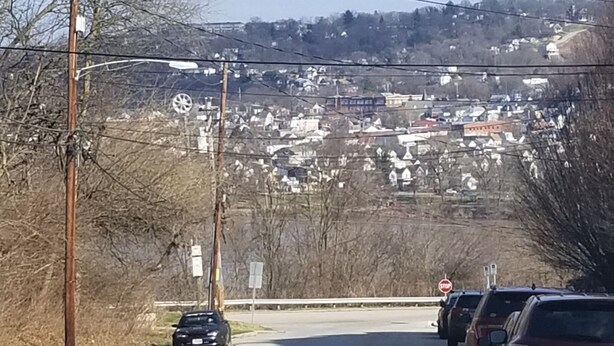 A road with parked cars, power lines, and a distant view of a town.