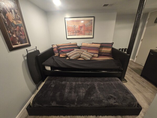 A bedroom with a bed, pillows, a framed picture, and a small table.
