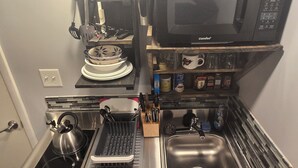 Cocina compacta con microondas, estufa, lavaplatos y diferentes utensilios.