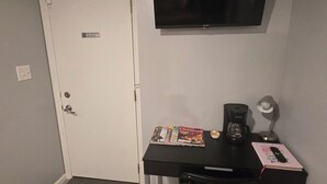 Una habitación pequeña con escritorio, silla, televisor y una puerta con un cartel de 'No Fumar'.