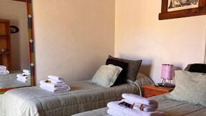 Une chambre d’hôtel avec deux lits, chacun agrémenté d’une serviette soigneusement pliée et d’un oreiller. On y trouve une tête de lit en bois, un tableau encadré au mur et un miroir avec un cadre coloré.