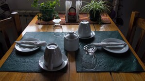 Une table à manger élégamment dressée, avec des assiettes, des tasses et un pichet en verre, entourée de chaises et de plantes en pot.