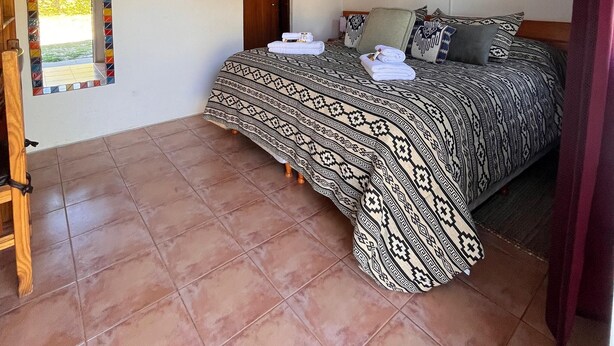 Une chambre avec deux lits, un plafond en bois, une fenêtre avec un cadre coloré, une porte portant le panneau «Interdiction de fumer» et un tableau encadré accroché au mur.