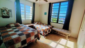 Ein Zimmer mit zwei Betten, einem Deckenventilator, großen Fenstern mit Vorhängen und Blick ins Freie.