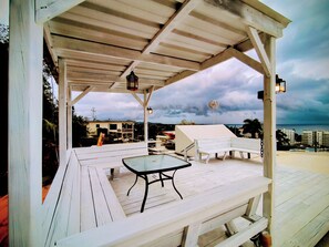 A covered outdoor seating area with a table and chairs, a view of the cityscape, and a cloudy sky.