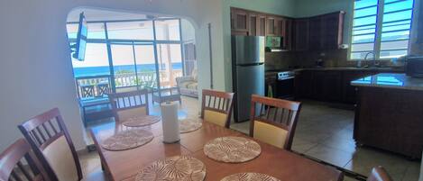 A dining area with a table set for four, a kitchen with modern appliances, and a view of the ocean through large windows.