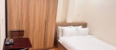 Une chambre avec une armoire en bois, un lit avec une literie blanche, une petite table avec des chaises et un plancher en bois.