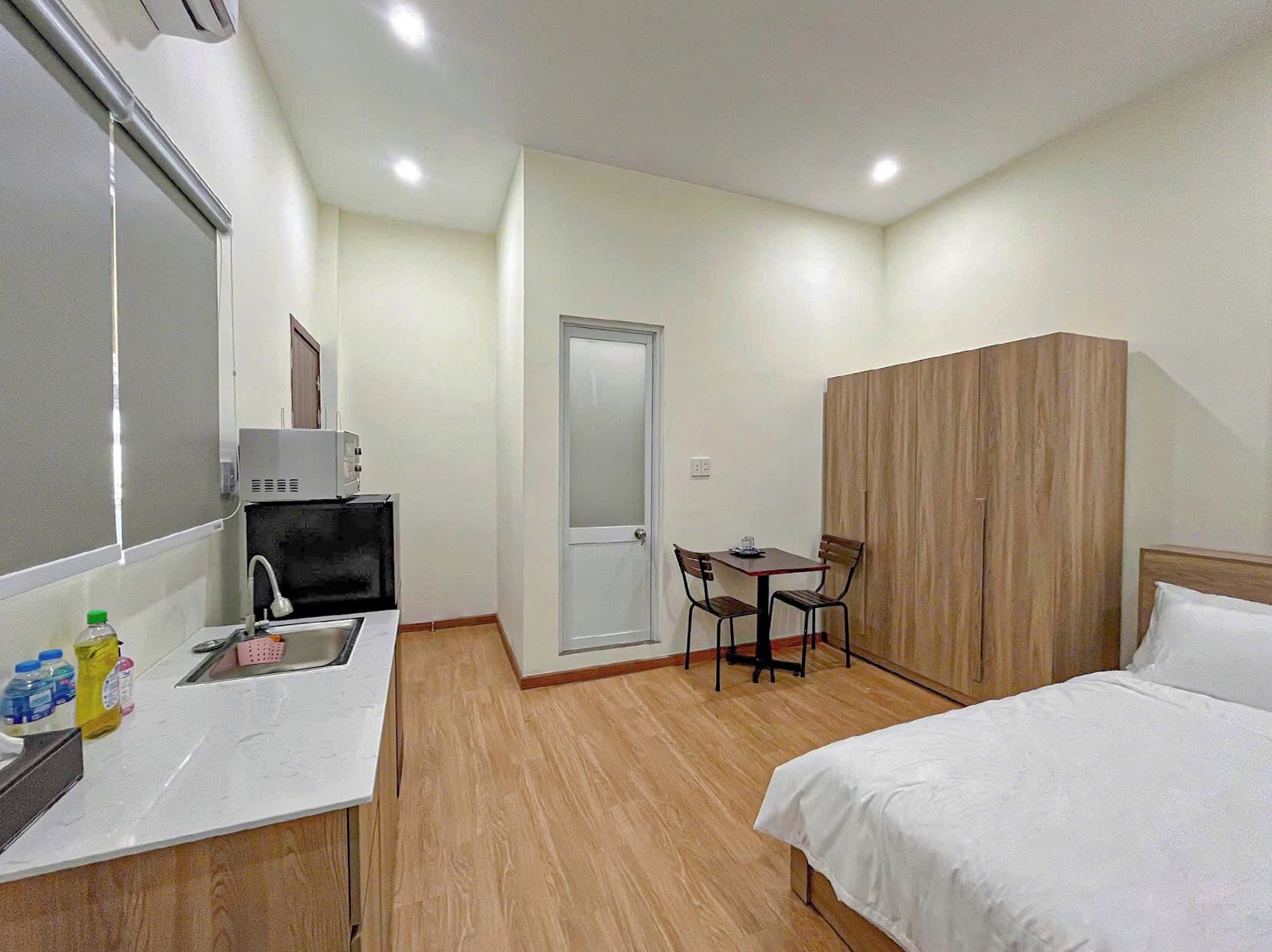 A compact hotel room with a kitchenette, a single bed, a wooden wardrobe, and a small table with chairs.