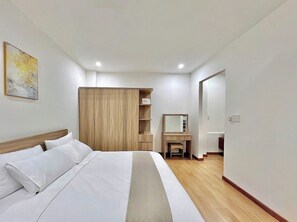 A hotel room with a bed, a wooden wardrobe, a desk with a mirror, and a small seating area. - Cozy Home Airport Ho Chi Minh (Ho Chi Minh City)