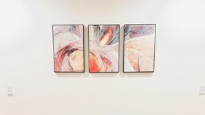 Ein braunes Ledersofa mit vier Kissen, ein schwarzer sechseckiger Couchtisch mit goldener Rahmen und drei abstrakte Gemälde an der Wand.