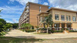 Ein mehrstöckiges Hotel mit flachem Dach, Balkonen und einem gepflasterten Eingangsbereich mit Palmen.