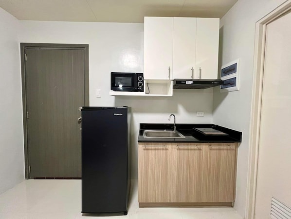 A compact kitchen with a refrigerator, microwave, and wooden cabinets.