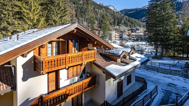A chalet with a balcony, wooden exterior, and snow-covered surroundings.