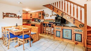 A cozy kitchen with wooden cabinets, a dining table with chairs, and a TV.