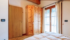 A bedroom with a wooden wardrobe, a bed with a white duvet, and a window with curtains.