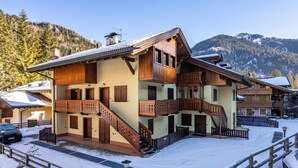 A multi-story wooden chalet with balconies, a staircase, and a snow-covered ground.