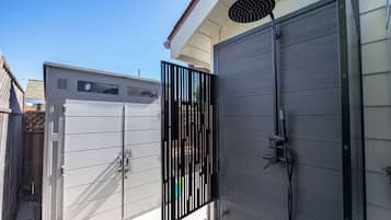 A modern outdoor shower enclosure with a metal gate, a hose, and a handheld showerhead.