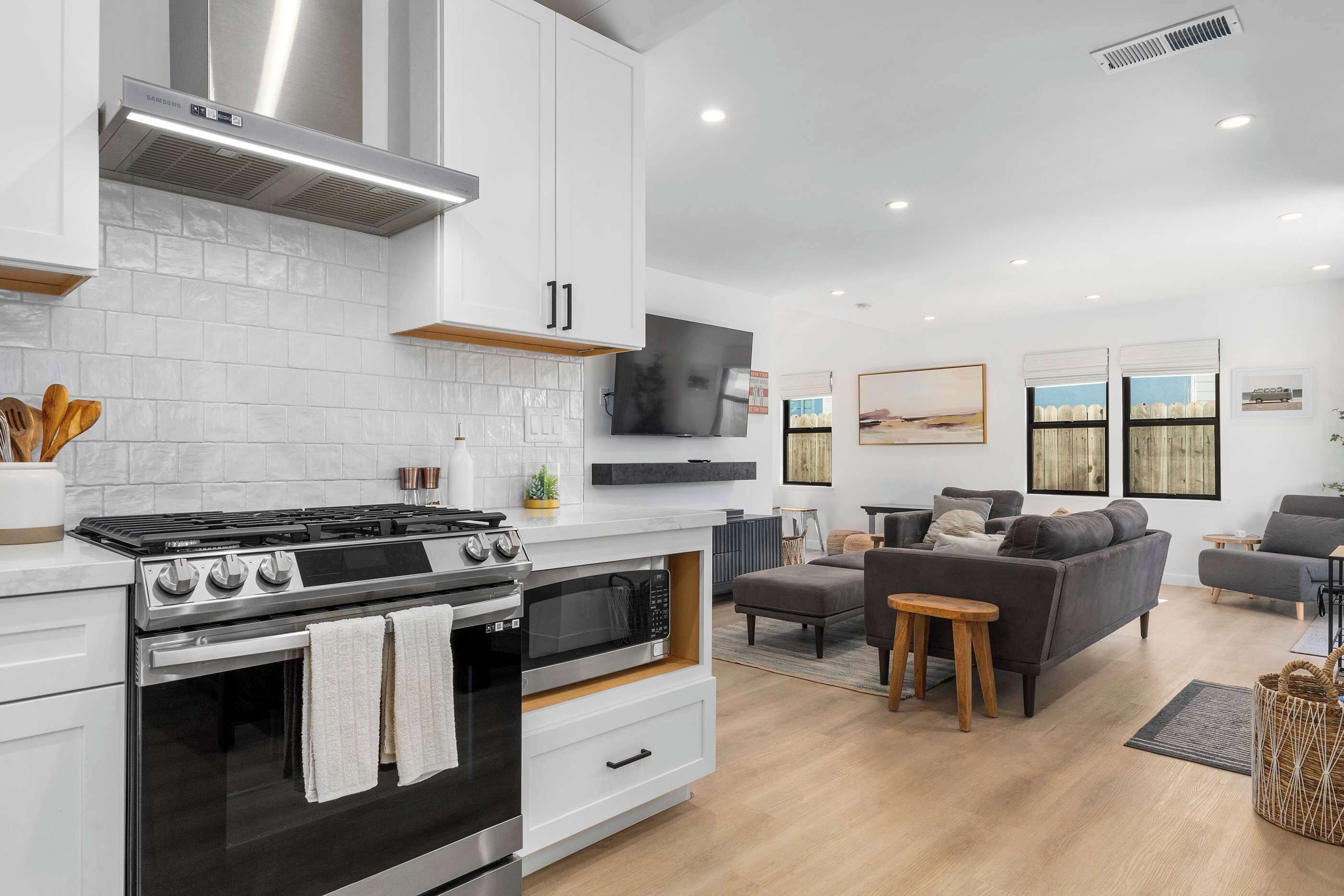 A modern kitchen with a gas stove, oven, and microwave, a dining area with a table and chairs, and a living room with a sofa and a TV.