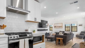 Una cocina moderna con estufa a gas, horno y microondas, un comedor con mesa y sillas, y una sala de estar con sofá y televisor.
