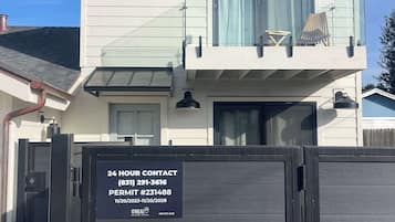 A two-story house with a gated entrance, a 24-hour contact sign, and a no parking sign.