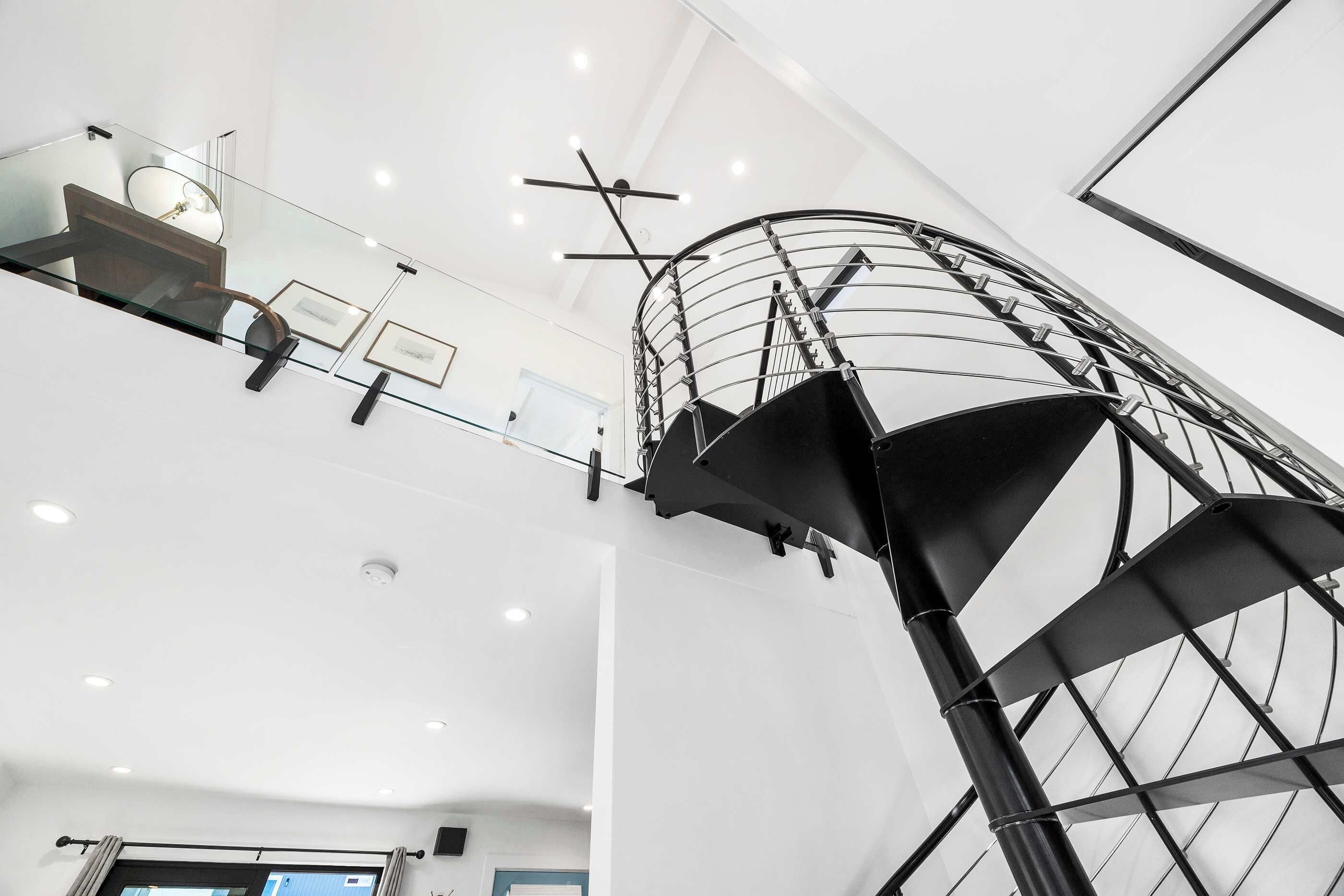 A modern interior with a spiral staircase, glass railings, and recessed ceiling lights.
