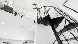 Un interior moderno con una escalera de caracol, barandillas de vidrio e iluminación empotrada en el techo.