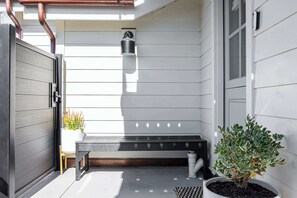 A covered outdoor area with a bench, potted plants, and a wall-mounted light fixture.