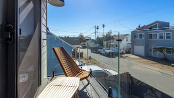 A balcony with a wooden chair and table, overlooking a street with houses and parked cars.