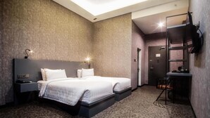 Una habitación de hotel moderna con dos camas, un escritorio, una silla y un televisor fijado a la pared.