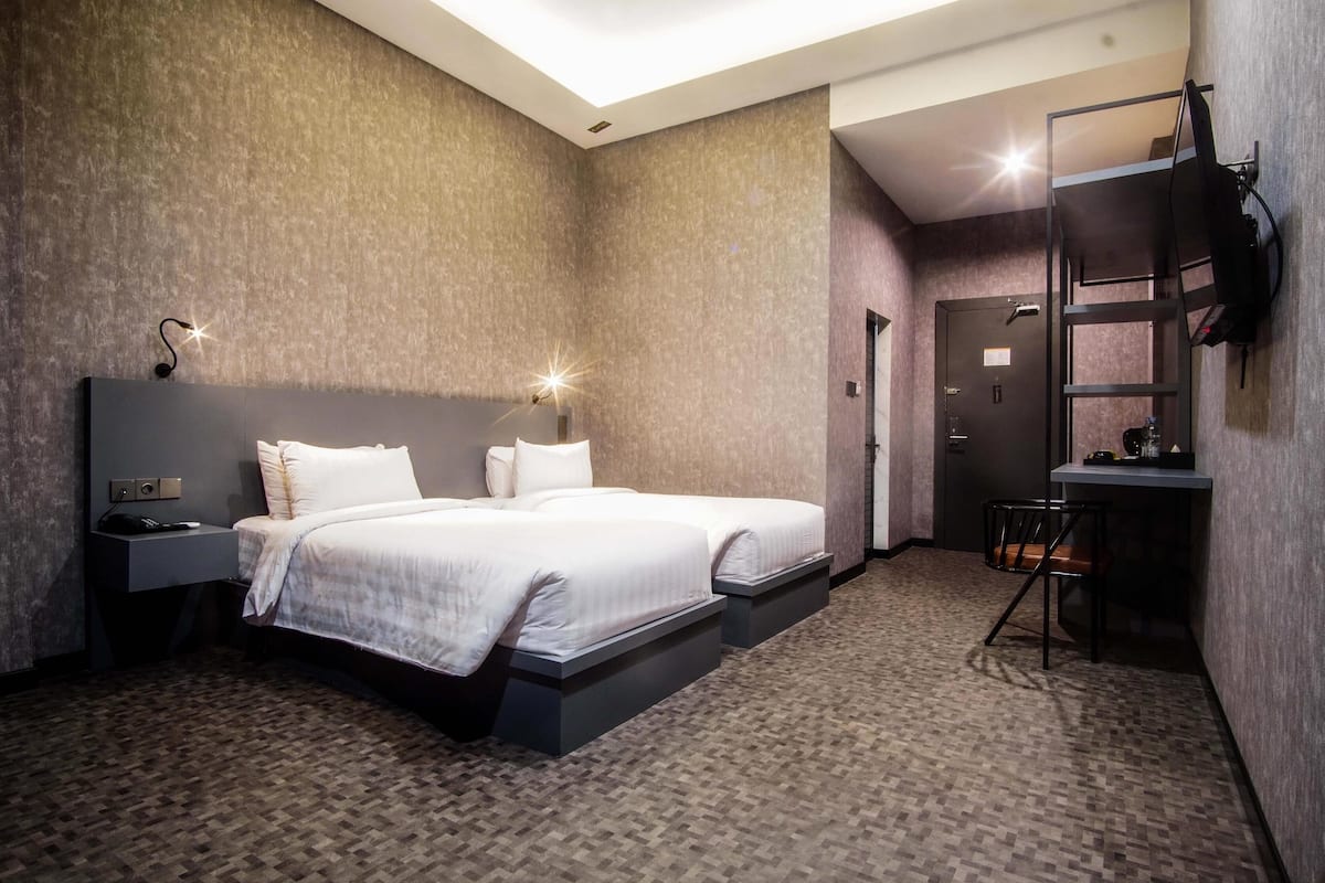 Een moderne hotelkamer met twee bedden, een bureau, een stoel en een televisie aan de muur.