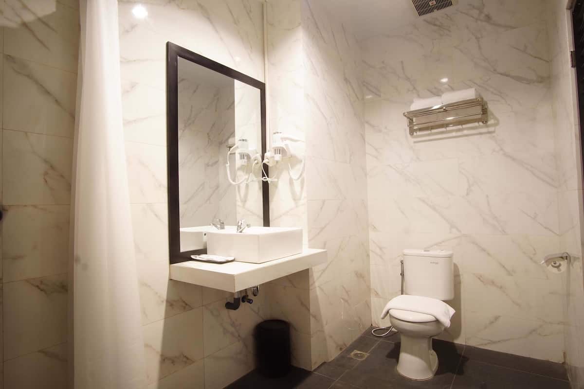 Een badkamer met een marmeren wand, een wastafel met spiegel, een toilet en een handdoekrek.