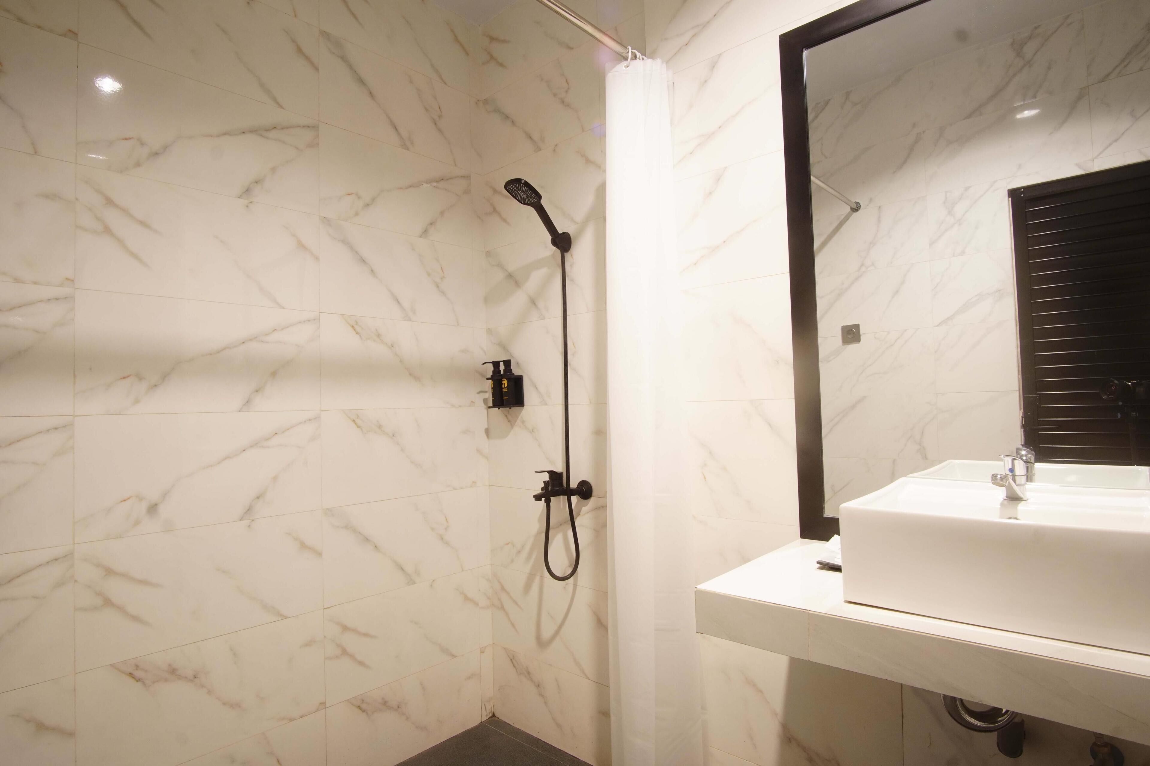 Un baño con un lavabo blanco, un espejo y una ducha con cabezal de ducha manual.
