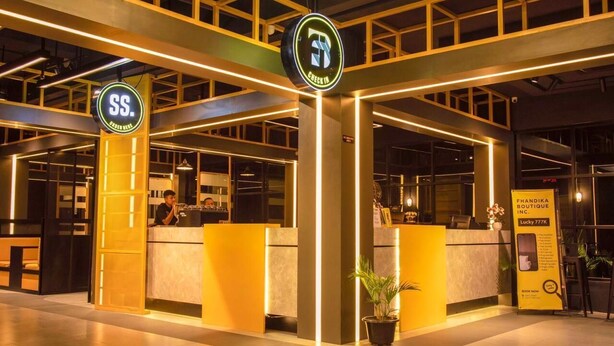 Zona de recepción de hotel con dos letreros visibles, un mostrador de recepción y una planta en maceta.