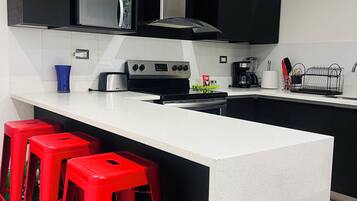 A modern kitchen with black cabinets, a white countertop, a stainless steel stove, and red bar stools.
