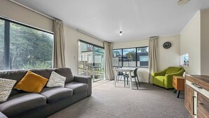 Een moderne woonkamer met een grijze bank, een groene fauteuil, een houten dressoir, en een eethoek met tafel en stoelen.