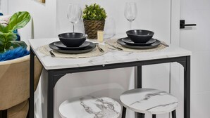 Une petite table à manger avec deux bols noirs et des verres à vin, une plante en pot et une chaise à motifs marbrés.