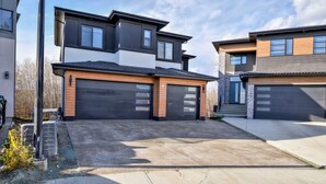 Une maison moderne à deux étages, dotée d’un garage, d’une allée et d’un petit jardin.