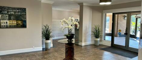 Un hall d’entrée agrémenté d’une grande plante en pot, d’une œuvre d’art accrochée au mur et d’une porte vitrée donnant sur l’extérieur.