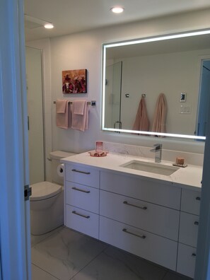 A modern bathroom with a large mirror, white cabinets, a toilet, and a shower.