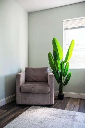 A corner room with a beige sofa, a white rug, and a large green plant. - We Connect Co-Living (St. Louis Park)